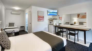 Habitación de hotel con cama, escritorio, silla, microondas, refrigerador pequeño y televisor.