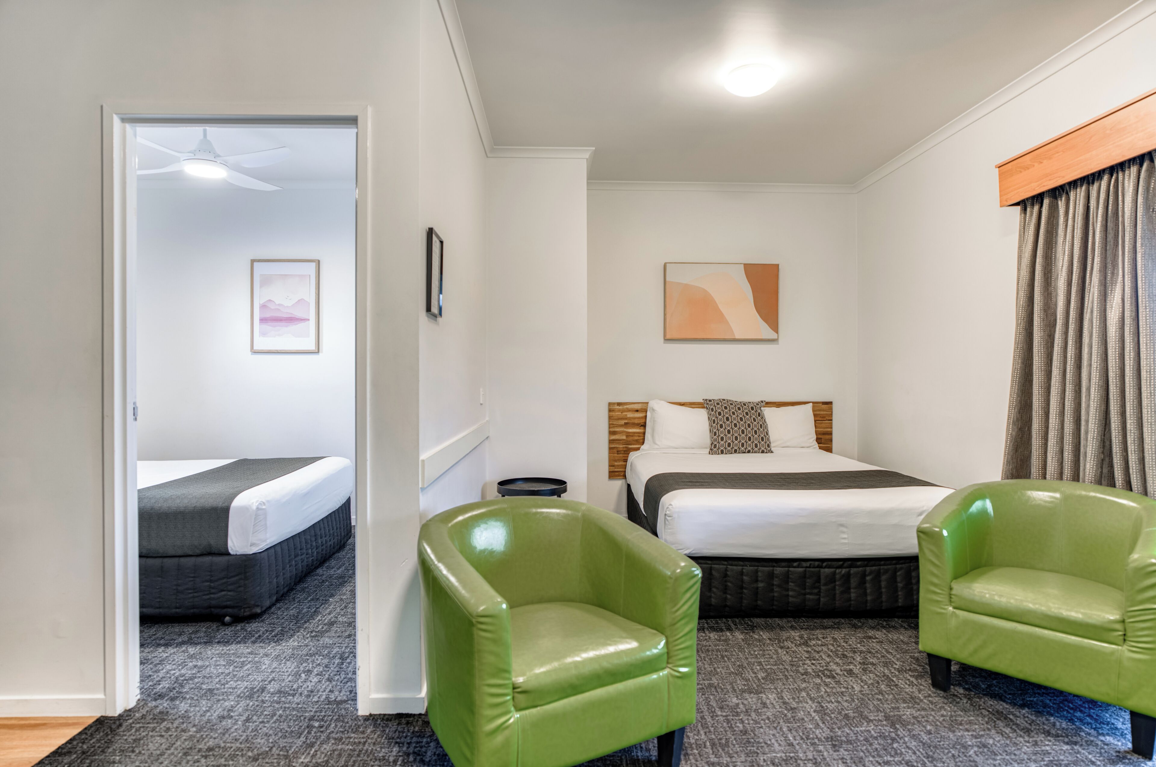 A hotel room with two beds, a green armchair, a headboard, and a painting on the wall.