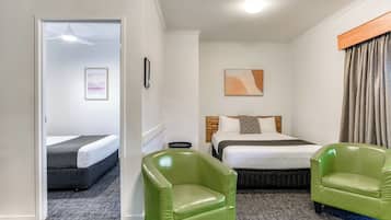 A hotel room with two beds, a green armchair, a headboard, and a painting on the wall.
