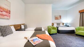 A hotel room with two beds, a green armchair, a nightstand, and a painting on the wall.