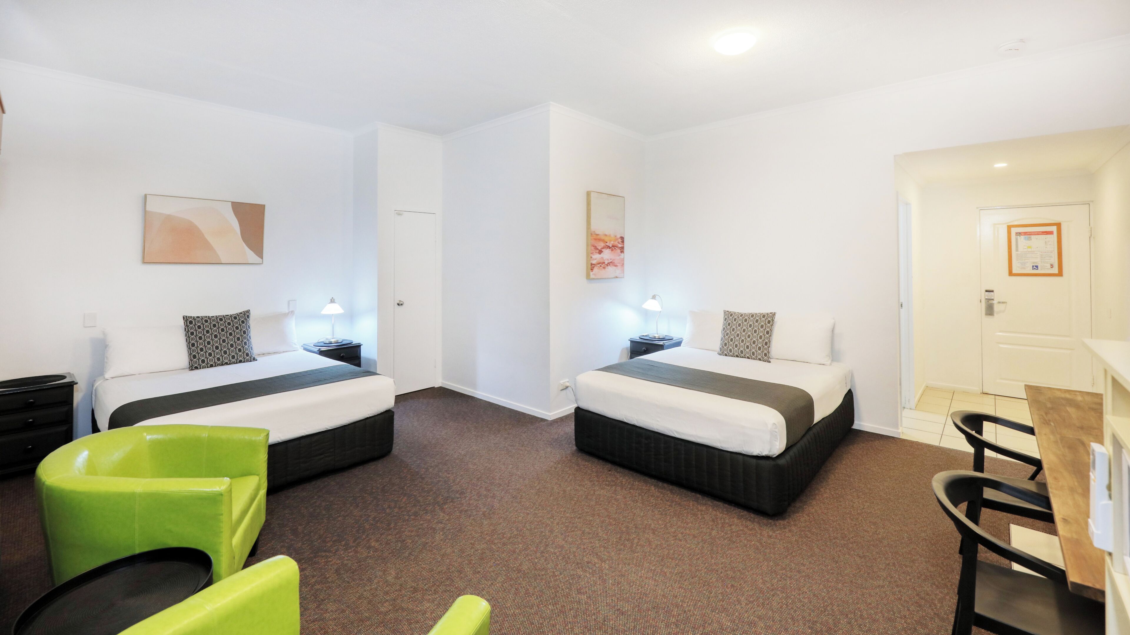 A hotel room with two beds, a desk, a chair, and a small seating area.