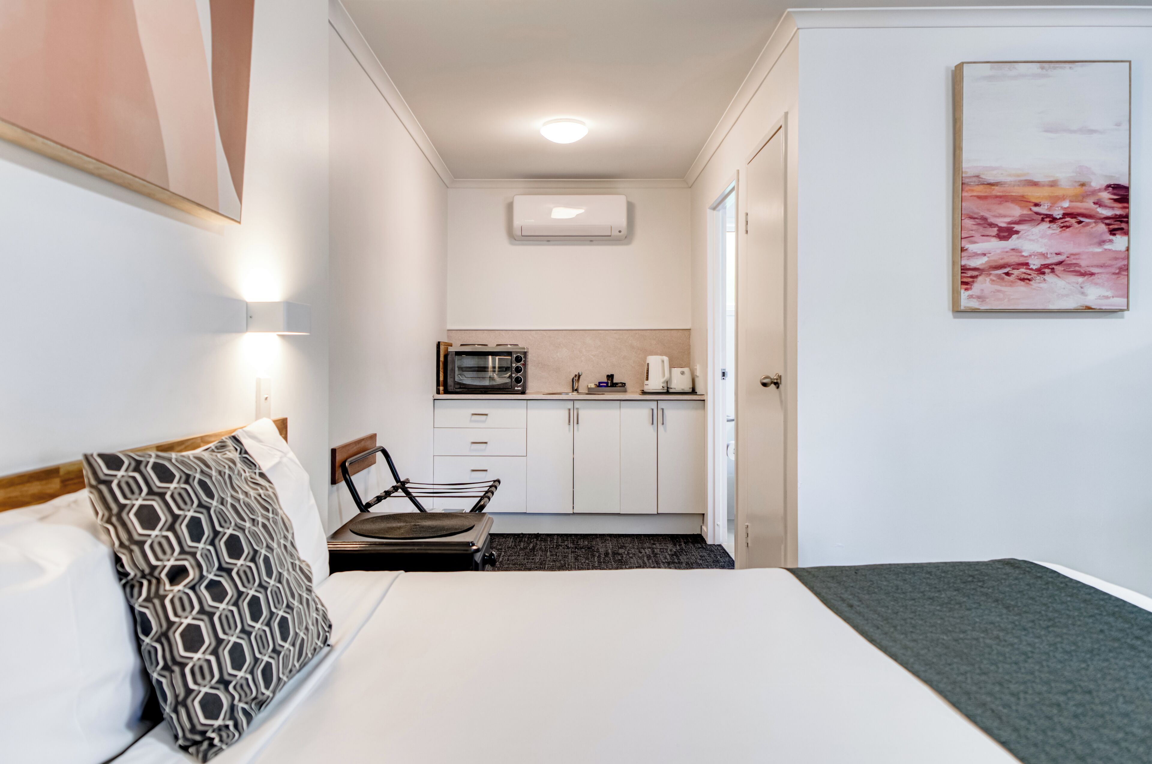 Una habitación de hotel con cama, una silla, kitchenette y puerta que da a otra habitación.