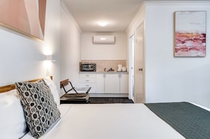 Una habitación de hotel con cama, una silla, kitchenette y puerta que da a otra habitación.