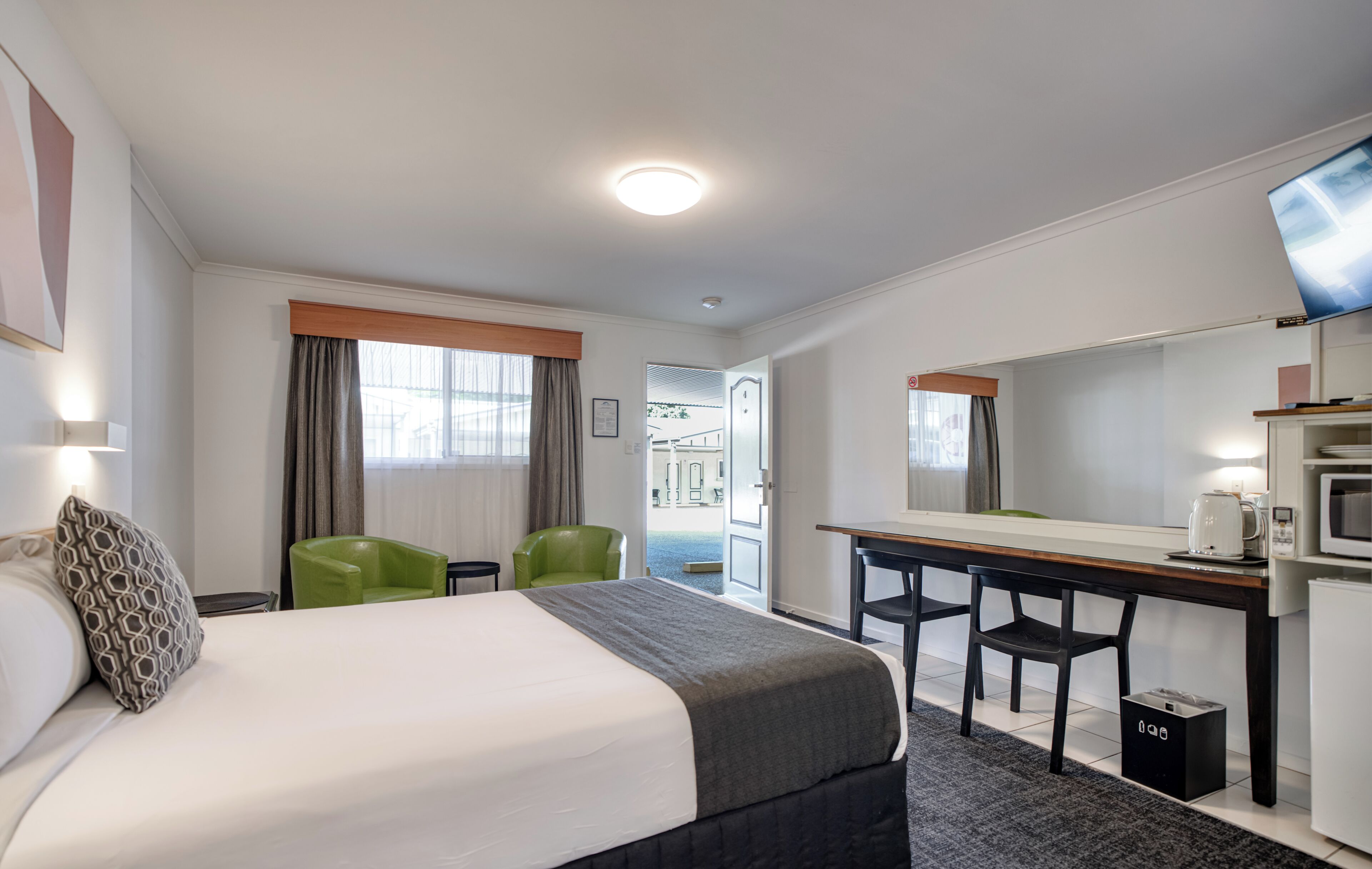 A hotel room with a bed, a desk, a chair, a television, and a view of the outside.