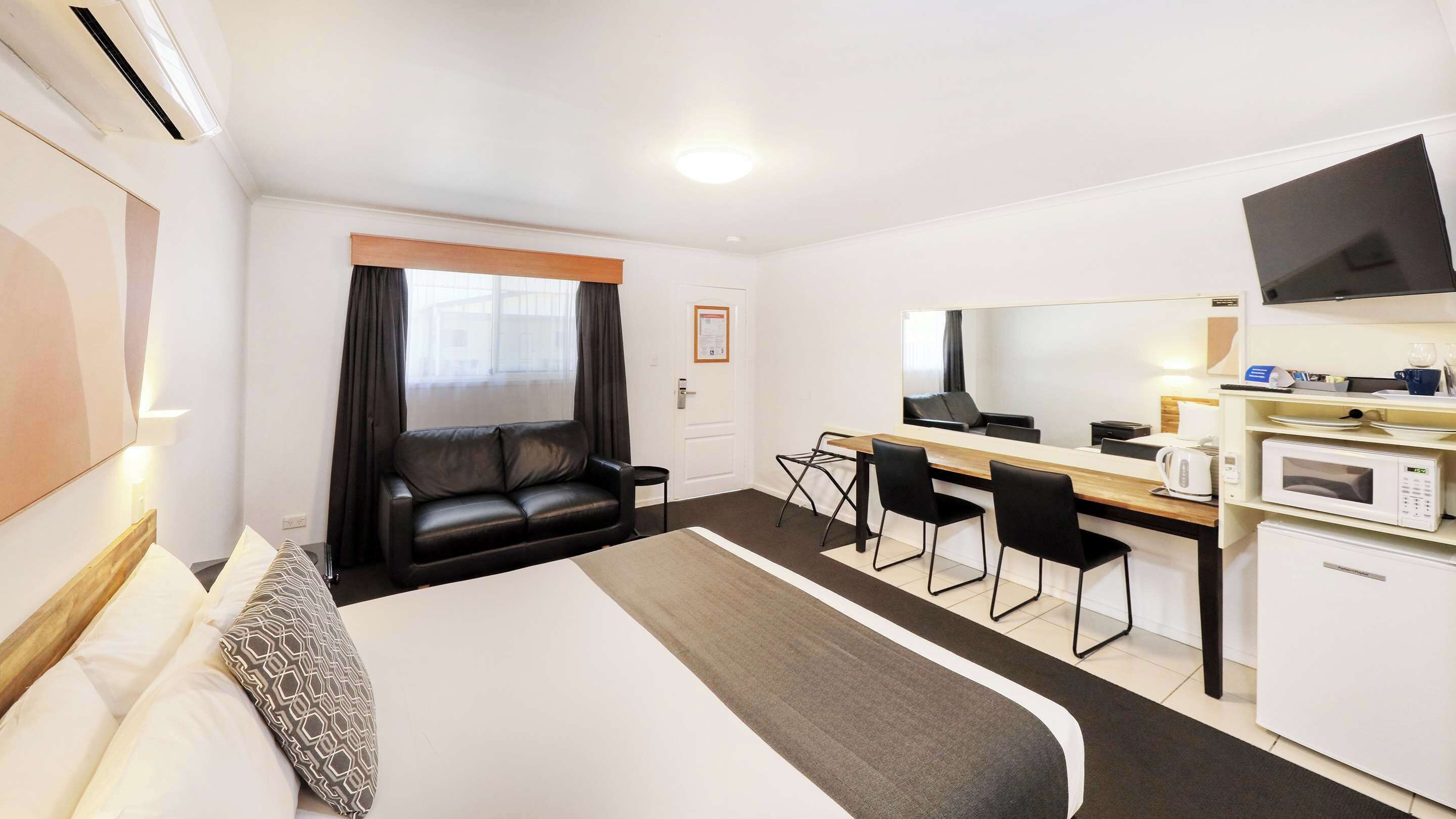 A hotel room with a bed, a desk, a chair, a microwave, and a TV.