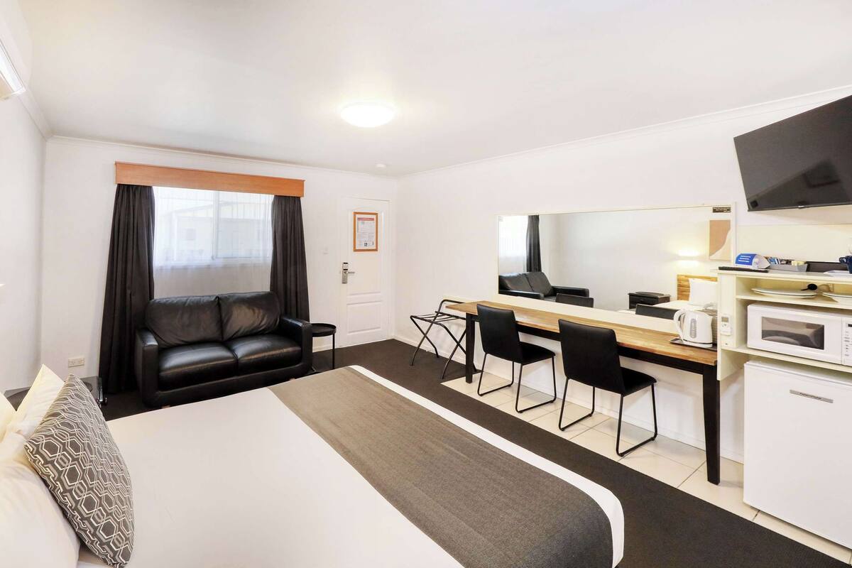 A hotel room with a bed, a desk, a chair, a microwave, and a TV.