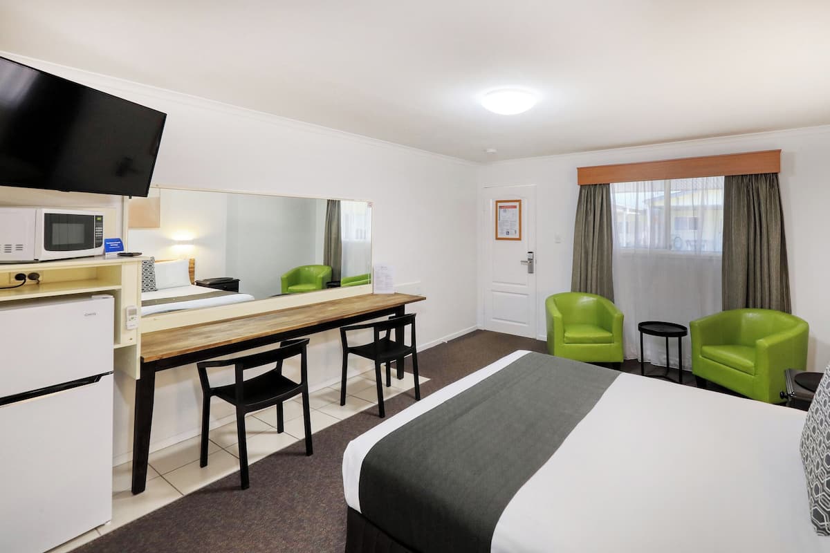 A hotel room with a bed, a desk, a chair, a television, a microwave, and a refrigerator.