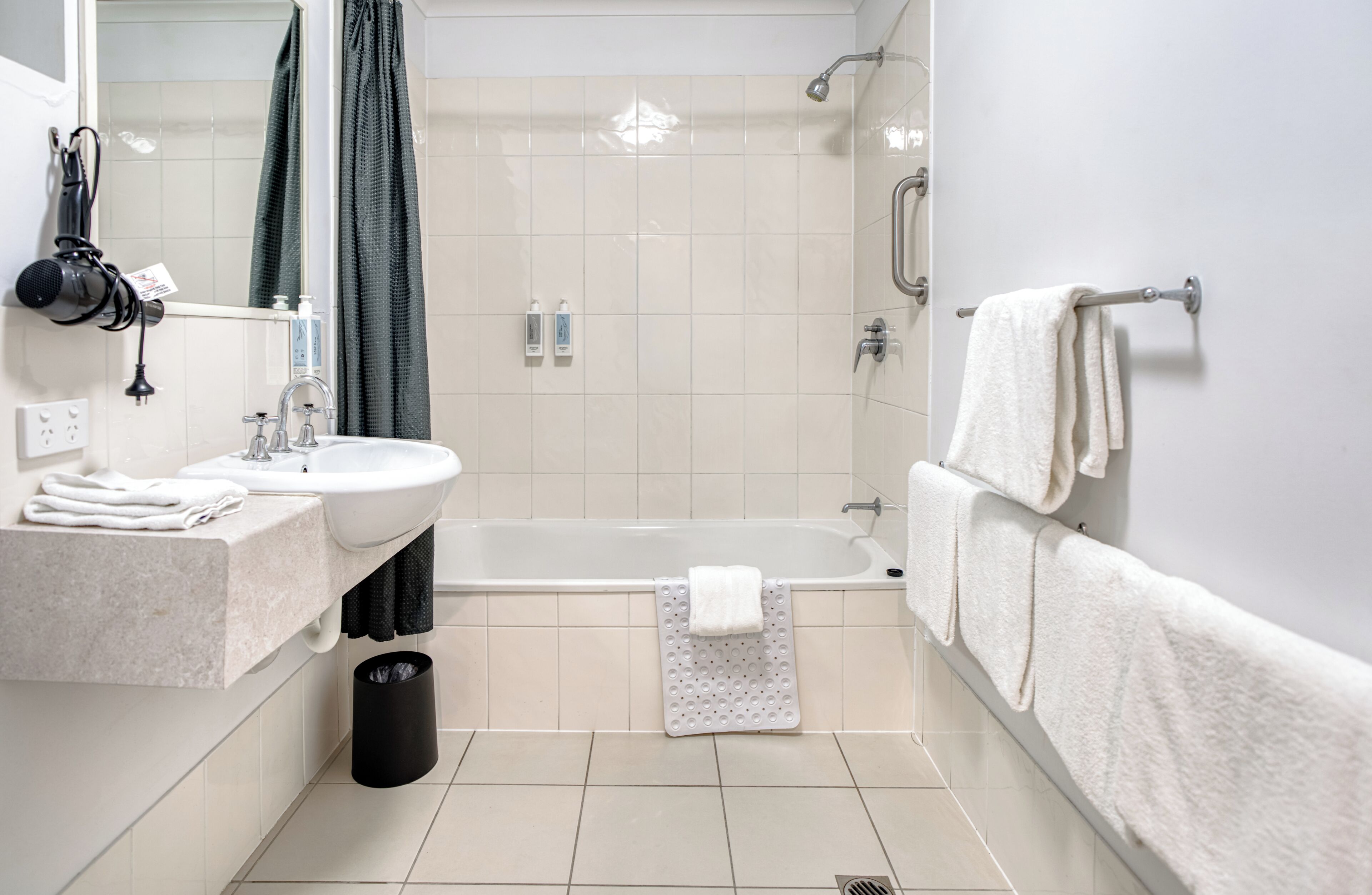 A modern bathroom with a sink, mirror, towel rack, and a shower area.
