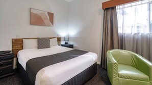 A hotel room with a bed, a nightstand, a lamp, a green chair, and a window with curtains. - Caboolture Gateway Motel (Caboolture)