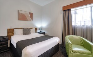 A hotel room with a bed, a nightstand, a lamp, a green chair, and a window with curtains. - Caboolture Gateway Motel (Caboolture)