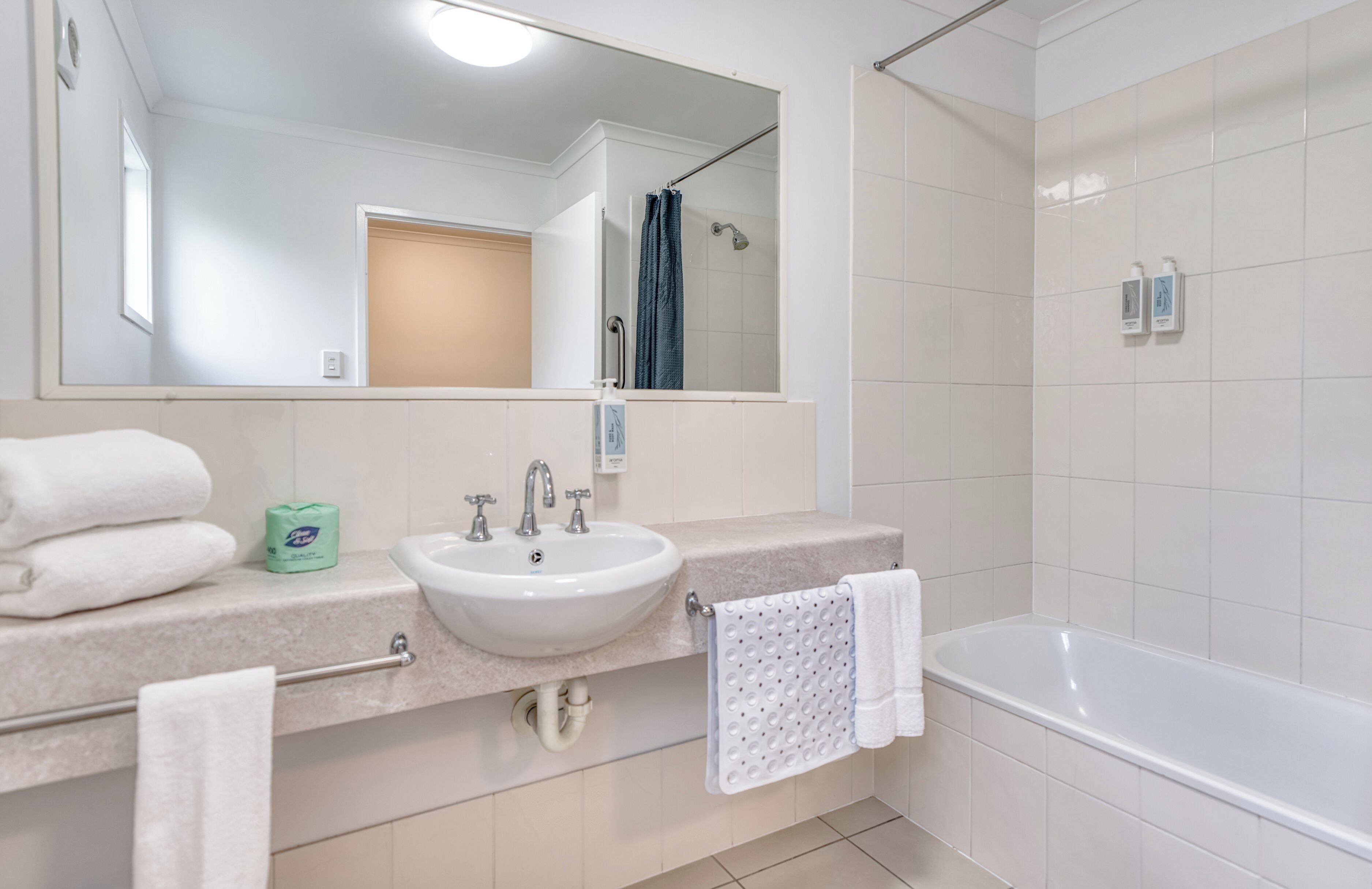 A modern bathroom with a white sink, two faucets, a mirror, a towel rack, and a bathtub.