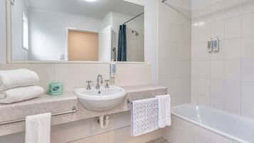 A modern bathroom with a white sink, two faucets, a mirror, a towel rack, and a bathtub.