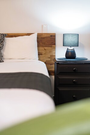 A neatly made bed with a wooden headboard, a bedside table with a lamp, and a wall-mounted light fixture. - Caboolture Gateway Motel (Caboolture)