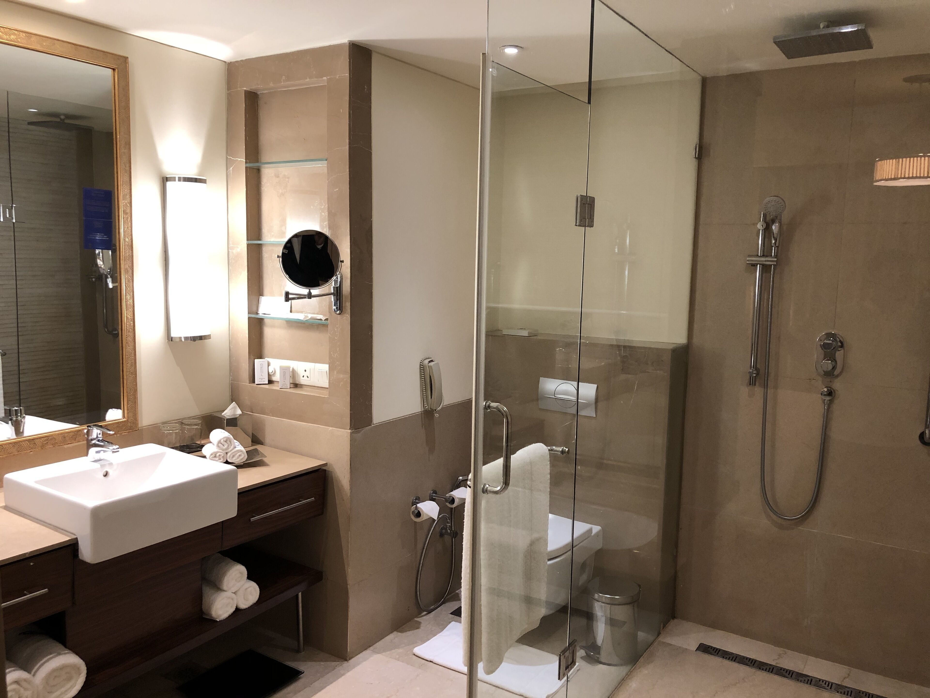 Une salle de bain moderne dotée d’une douche à parois de verre, d’un grand miroir et d’un meuble-lavabo avec un espace pour ranger les serviettes.
