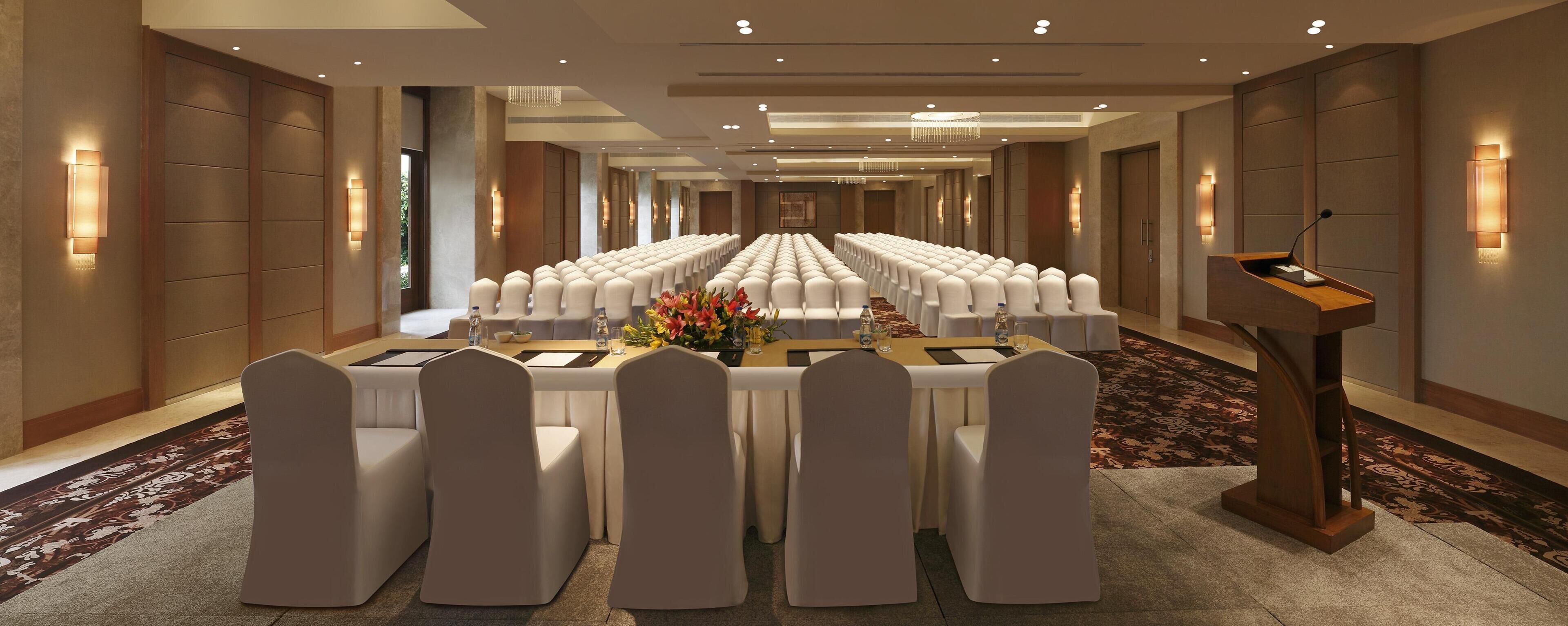 A conference room with rows of white chairs, a podium, and a floral centerpiece.