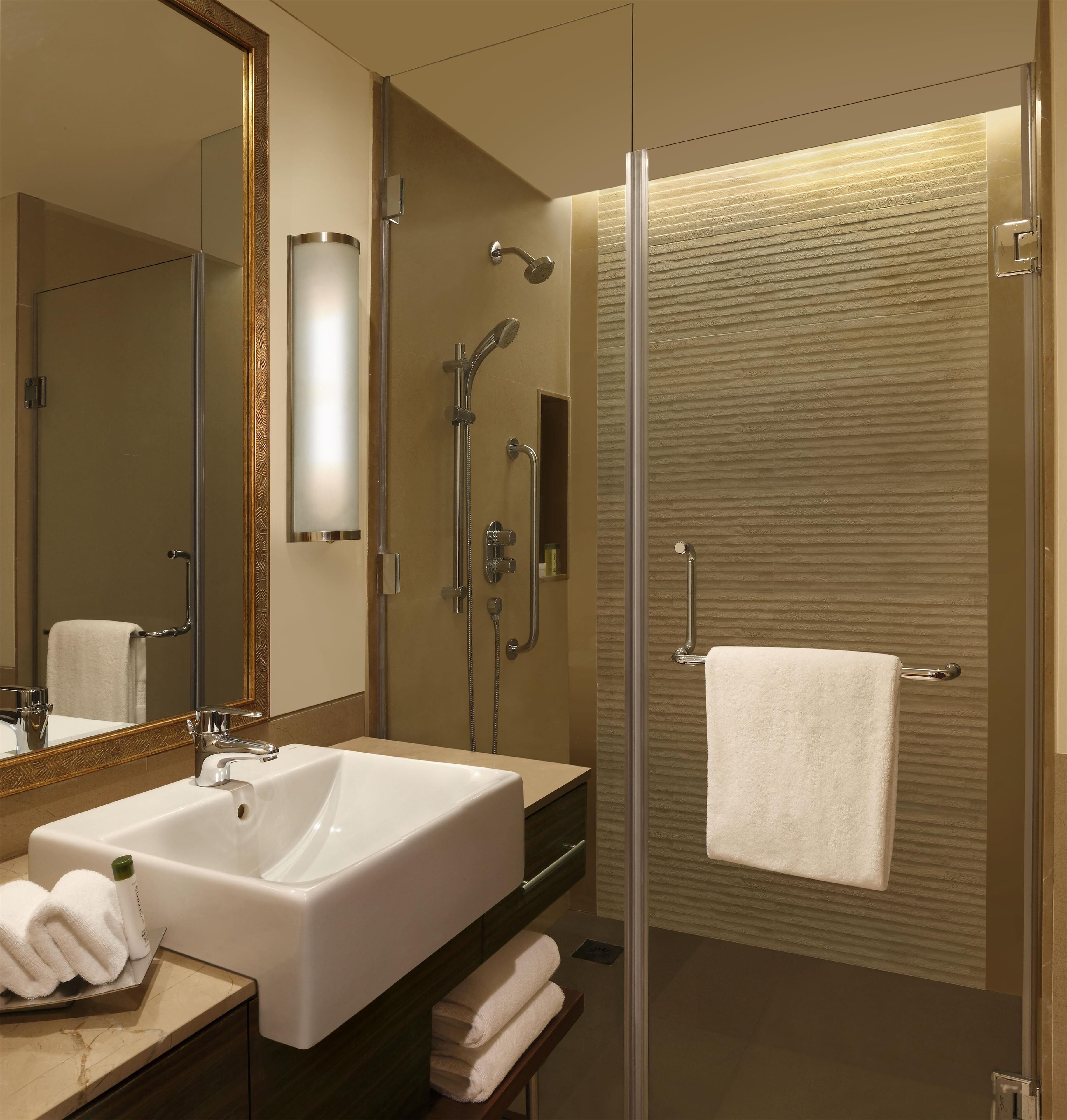 A modern bathroom with a large mirror, a white sink, a glass-enclosed shower, and a towel rack.