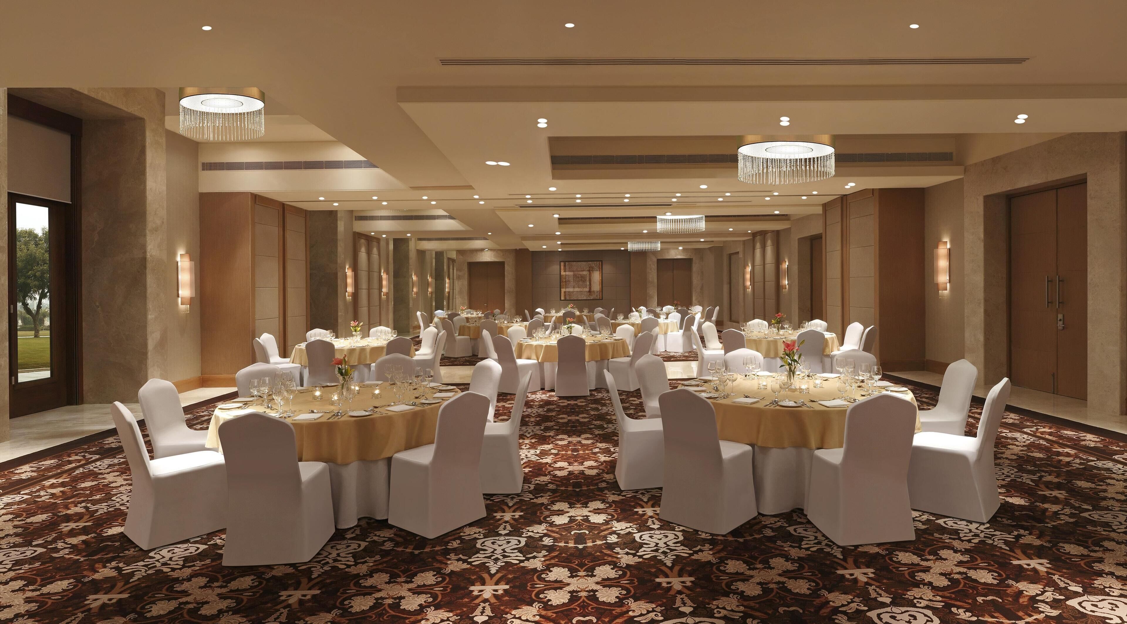 Un salón de banquetes con mesas redondas, sillas blancas, candelabros y una alfombra estampada.