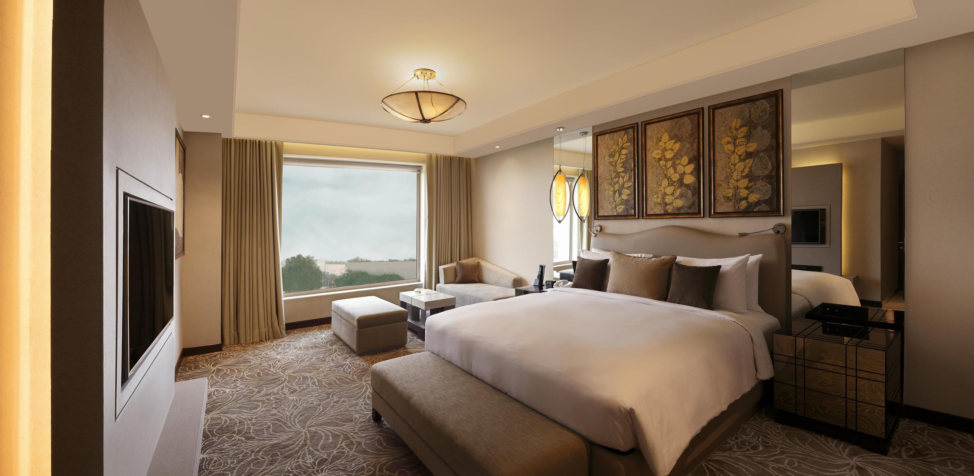 A hotel room with a large bed, a TV, a desk, a chair, and a window with curtains.