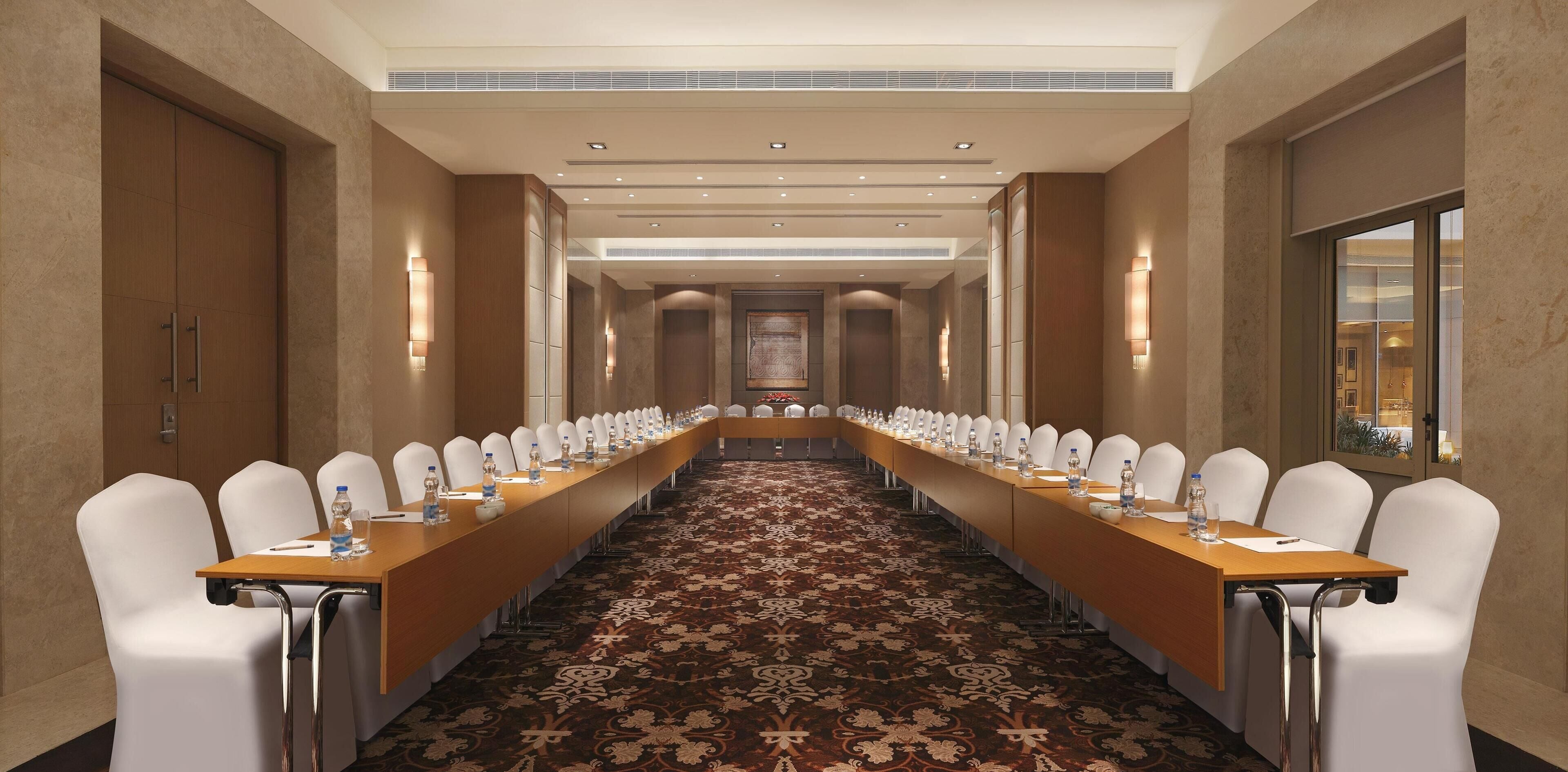 A conference room with a long table, white chairs, and a patterned carpet.