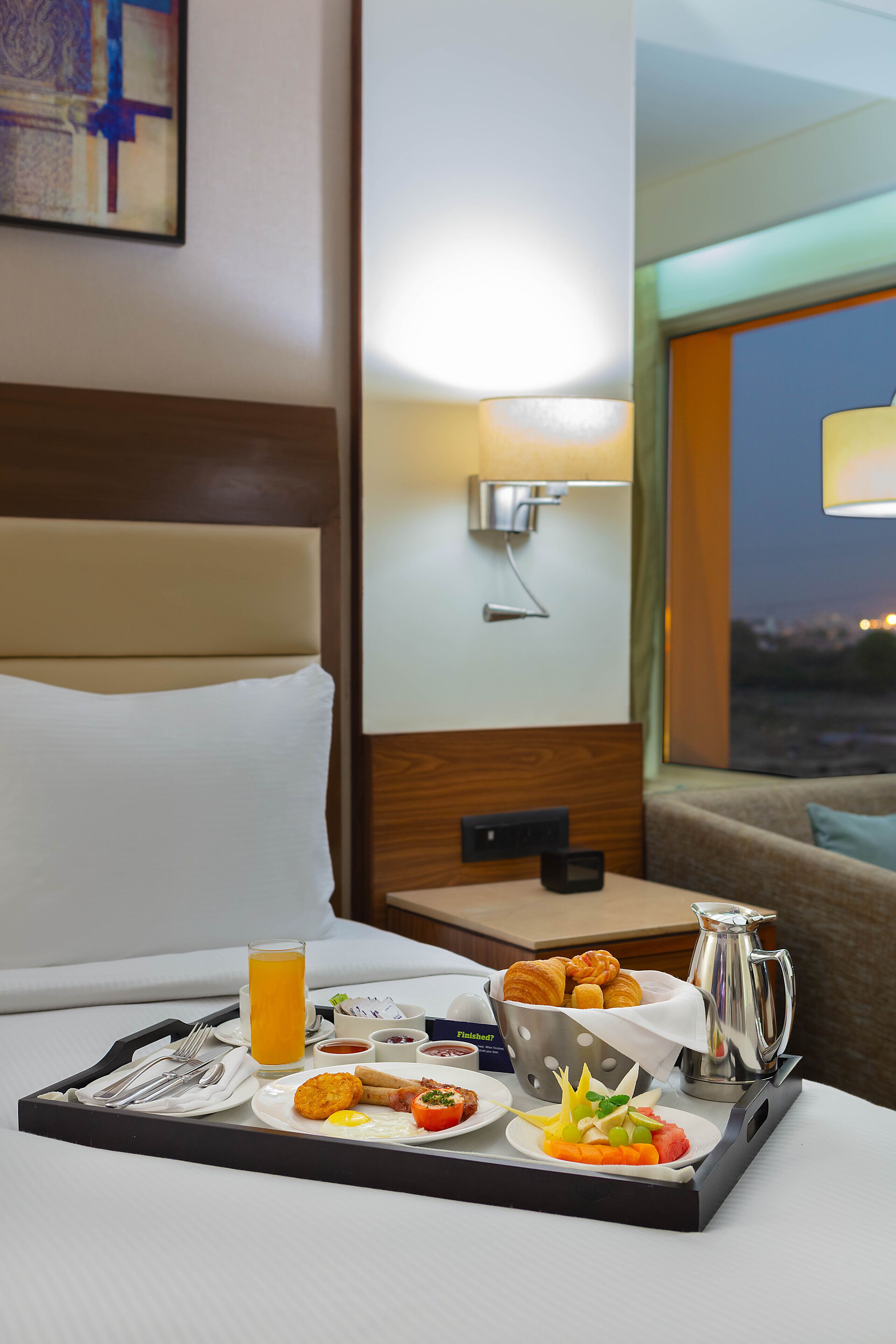 A hotel room with a breakfast tray on the bed, including croissants, eggs, and fruit.