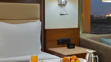Habitación de hotel con una bandeja de desayuno en la cama, que incluye croissants, huevos y fruta.