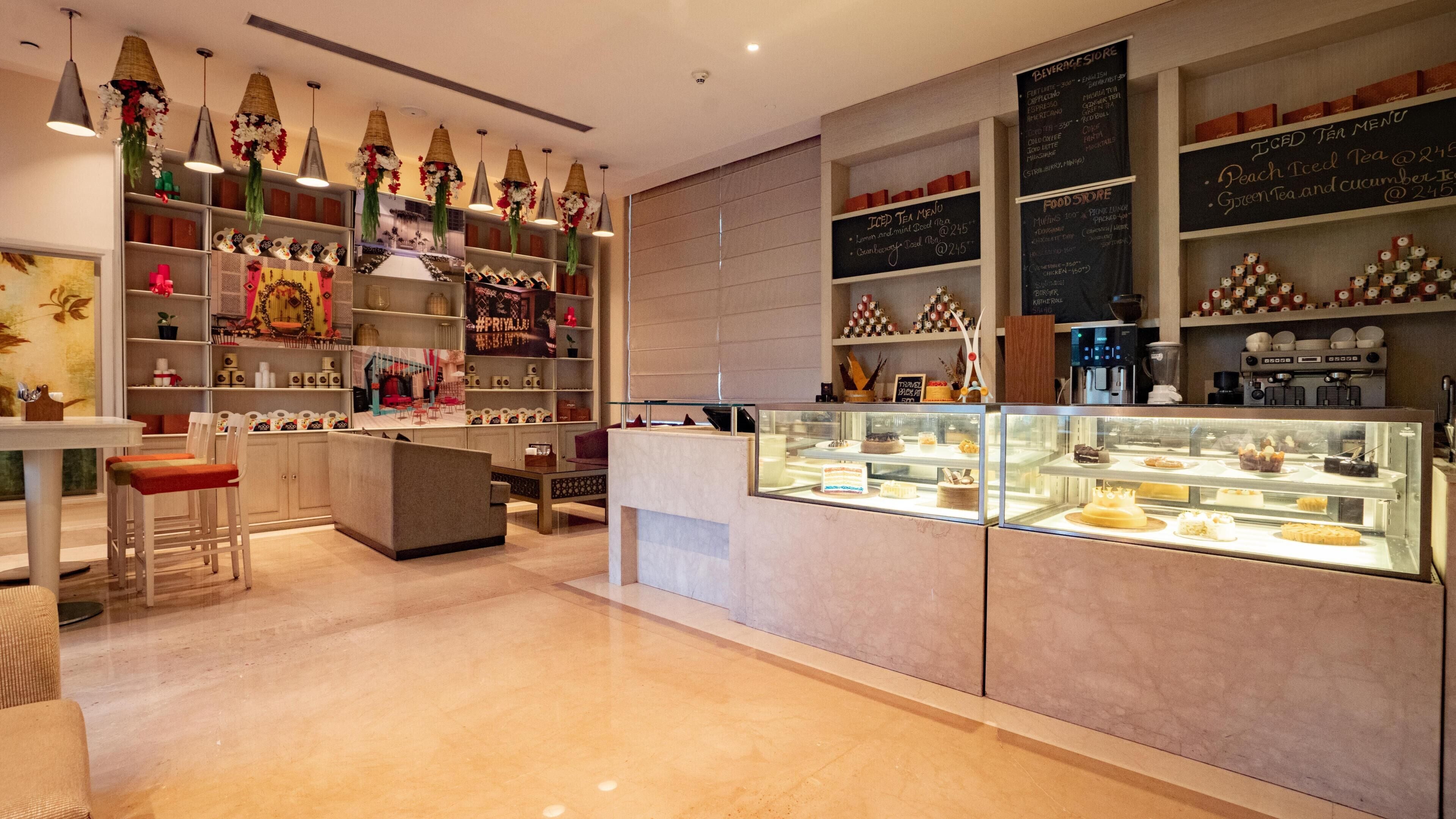 A modern cafe interior with a counter displaying pastries, shelves with various items, and hanging decorative lights.