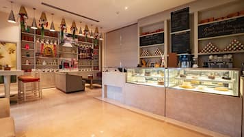 A modern cafe interior with a counter displaying pastries, shelves with various items, and hanging decorative lights.