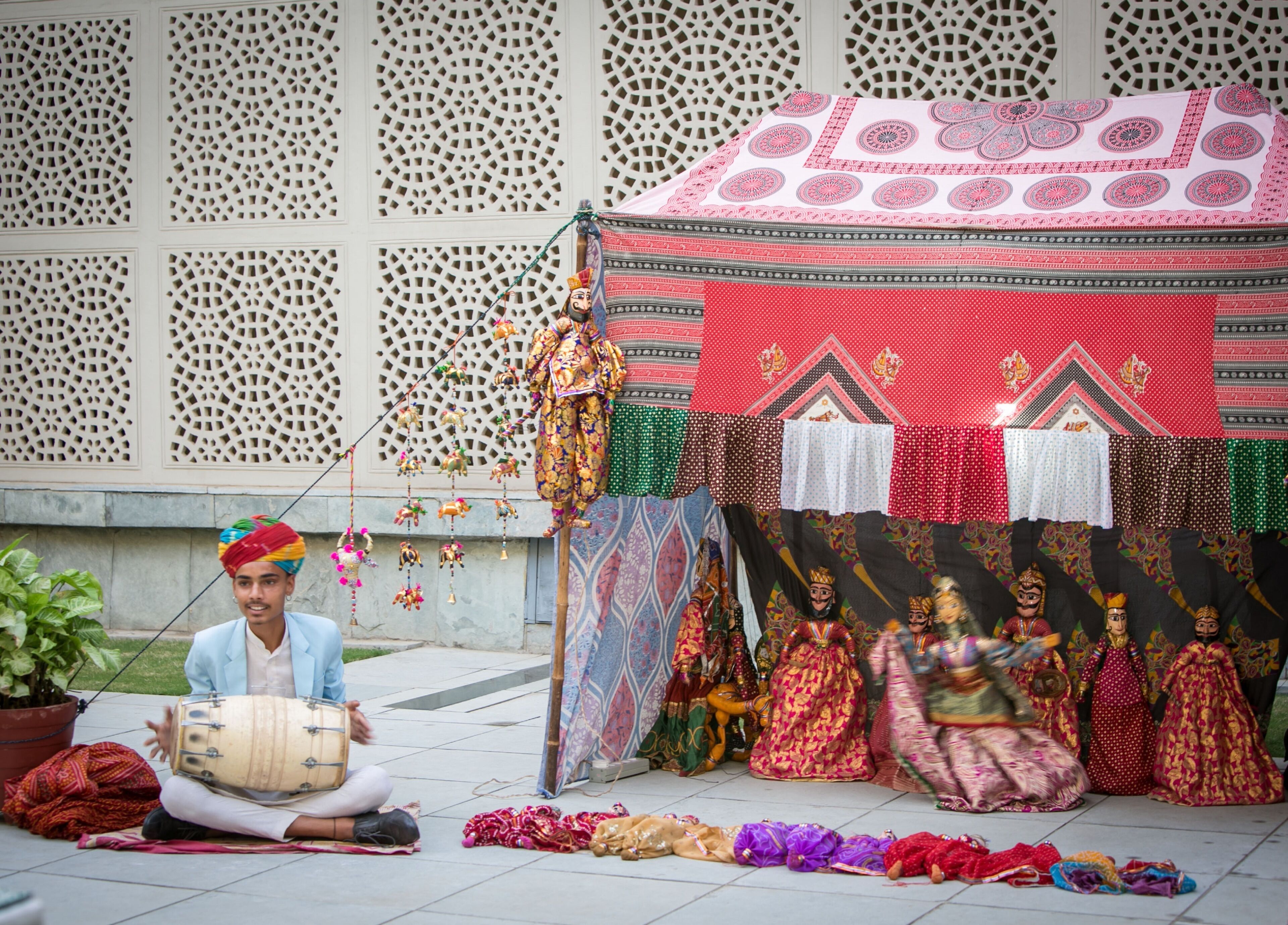 A person playing a drum, a tent with colorful fabrics, and a decorative wall with intricate patterns.