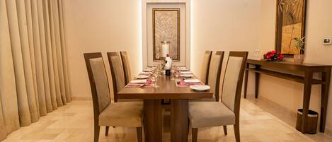 Comedor con una larga mesa dispuesta para seis comensales, sillas a los lados, un jarrón con flores y una obra de arte enmarcada en la pared.