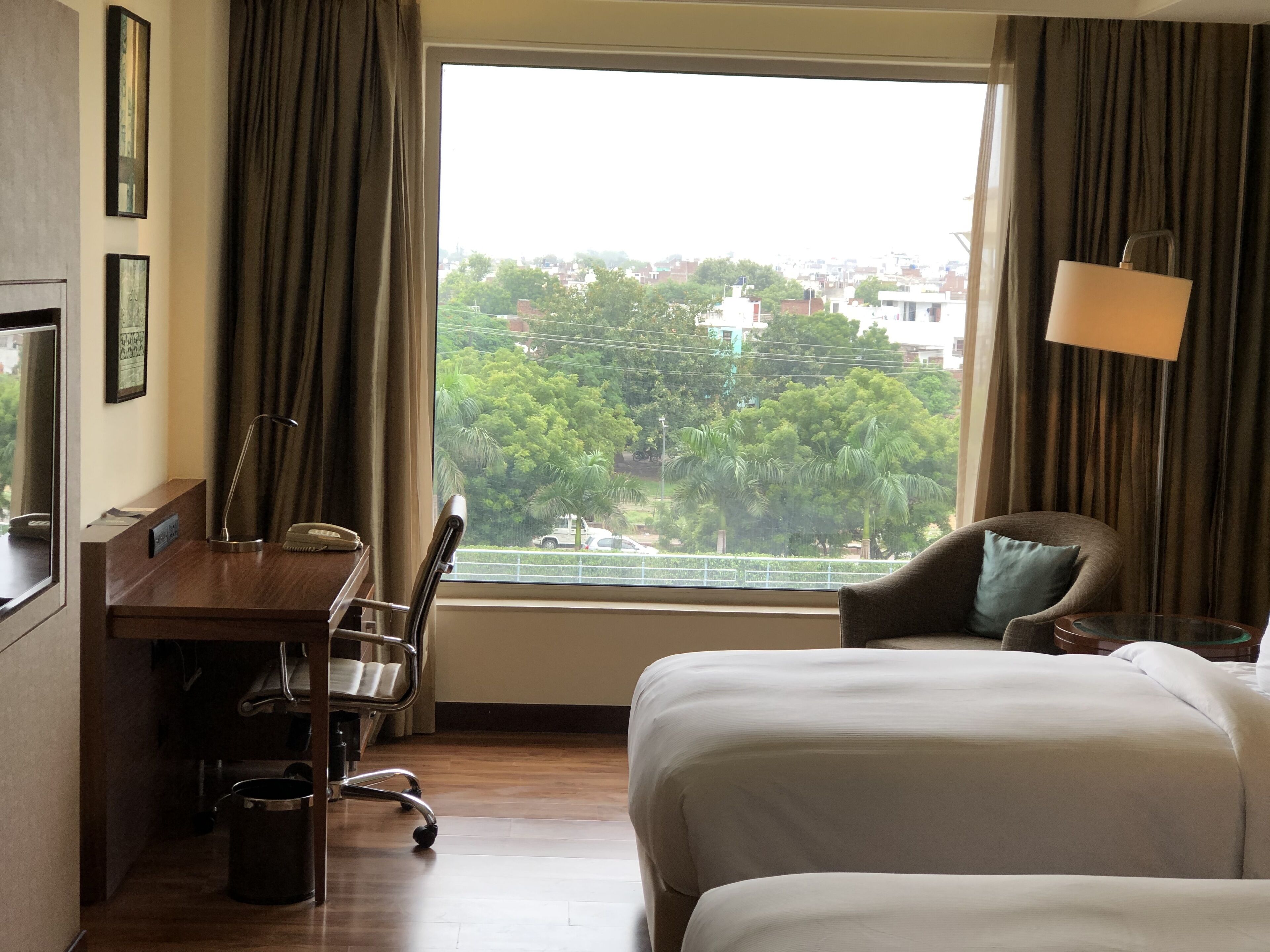 A hotel room with a large window, a desk, a chair, and a bed.