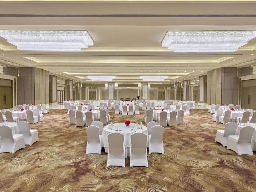 A large, well-lit banquet hall with round tables and white chairs, arranged in a symmetrical layout.