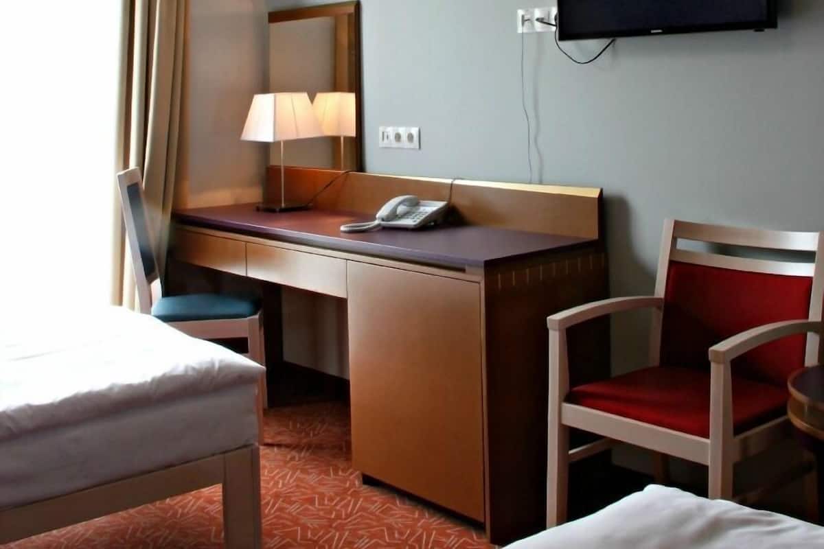 Ein Hotelzimmer mit Bett, Schreibtisch, Stuhl, Fernseher und Spiegel.