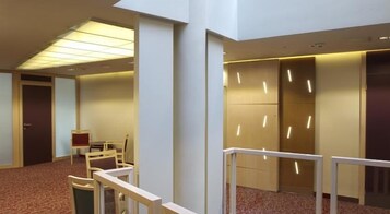 Um lobby de hotel moderno, com teto alto, iluminação embutida e área de estar com cadeiras e uma mesa pequena.