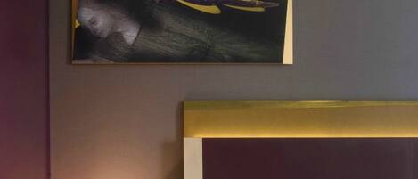 A hotel room with a bed, a nightstand with a lamp, and a painting on the wall.