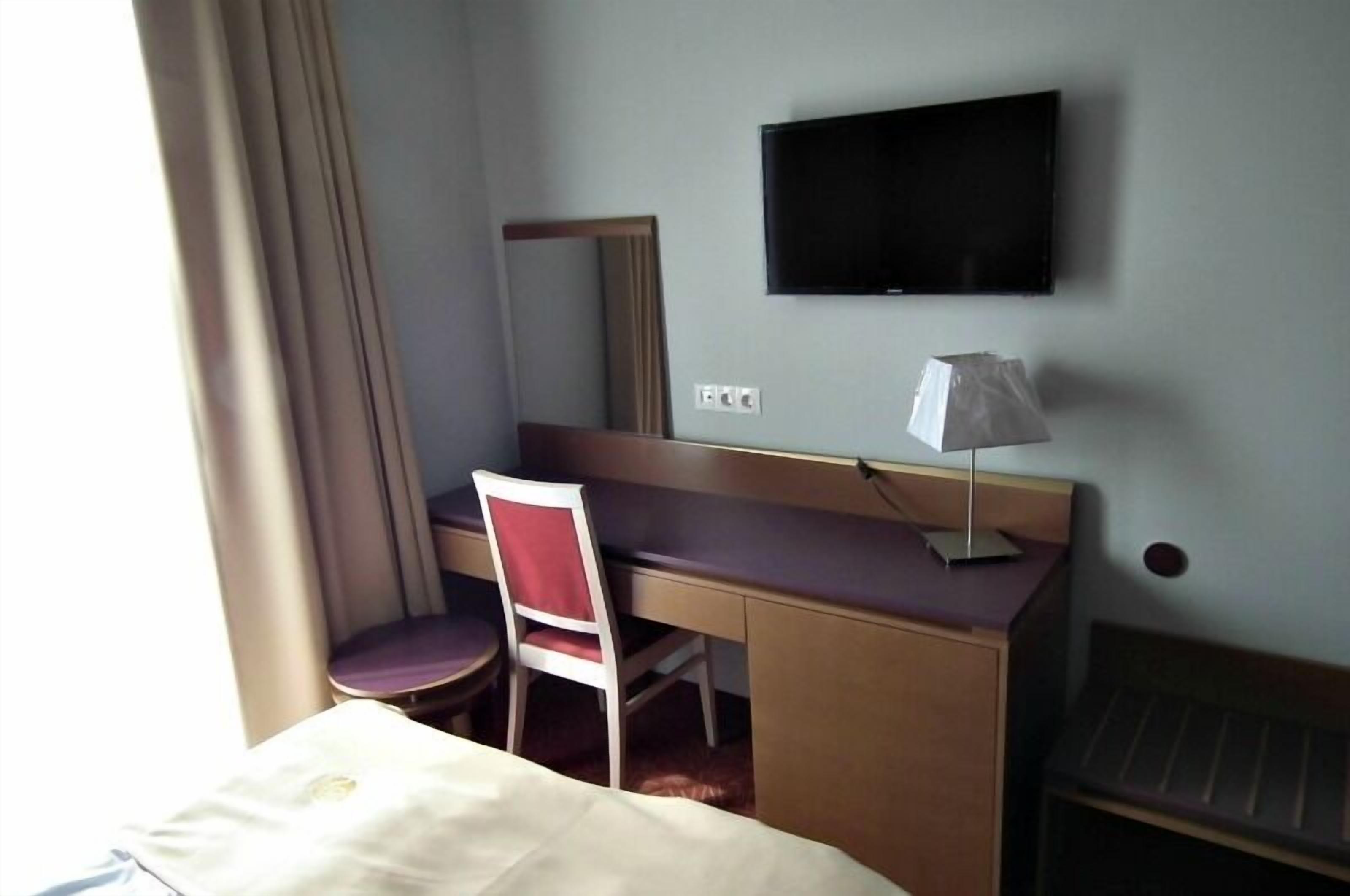 Una habitación de hotel con una cama, un escritorio con una silla, un televisor y una lámpara.