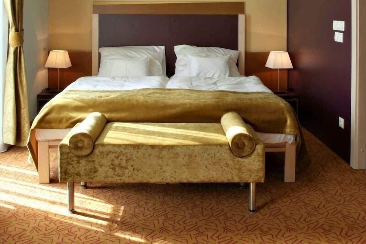 Ein Hotelzimmer mit einem großen Bett, zwei Nachttischlampen, einem Bild an der Wand und einem gemusterten Teppich.