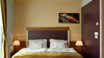 A hotel room with a large bed, two bedside lamps, a painting on the wall, and a patterned carpet.