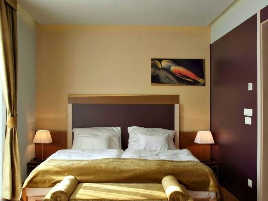 A hotel room with a large bed, two bedside lamps, a painting on the wall, and a patterned carpet.