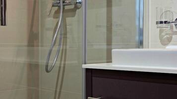 Une salle de bain moderne avec une douche à l’italienne en verre, un lavabo blanc et un meuble-lavabo aux tons foncés.