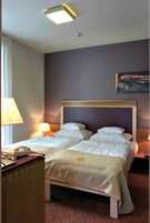Quarto de hotel com cama de casal, luminárias de cabeceira, escrivaninha com telefone e um quadro na parede.