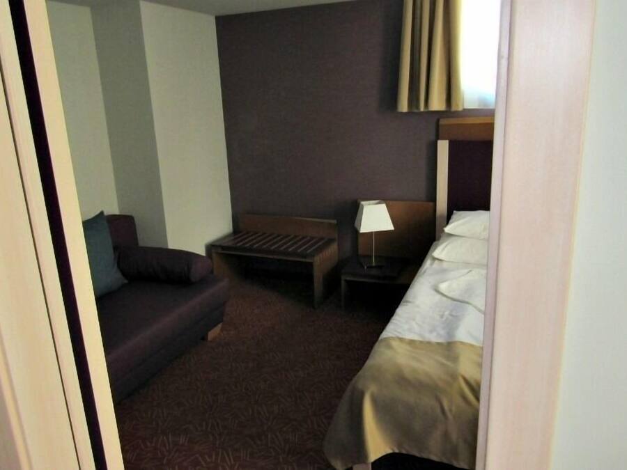 Habitación de hotel con cama, escritorio pequeño, silla, sofá y lámpara.