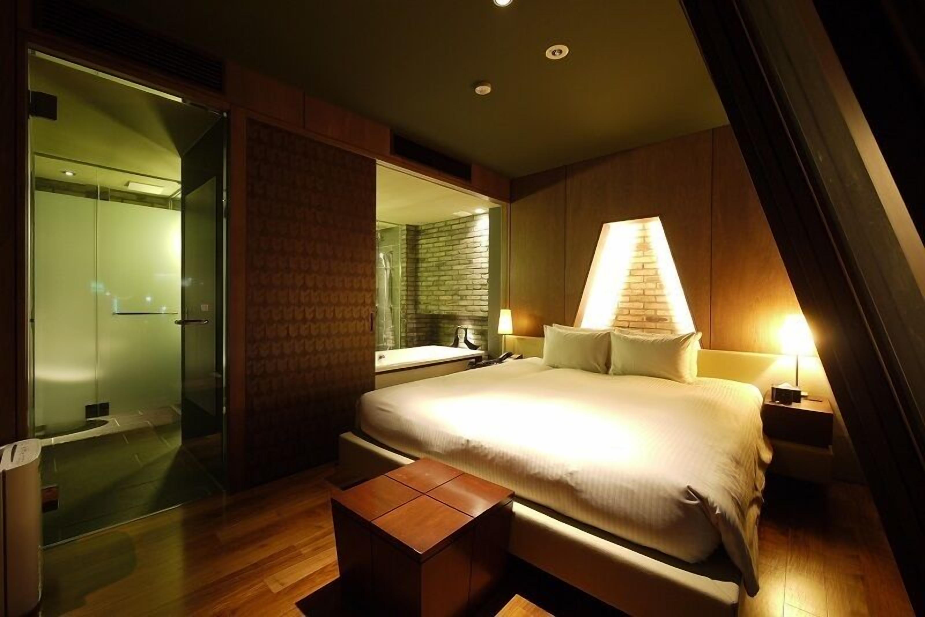 A modern hotel room with a large bed, a glass shower enclosure, and a wooden floor.