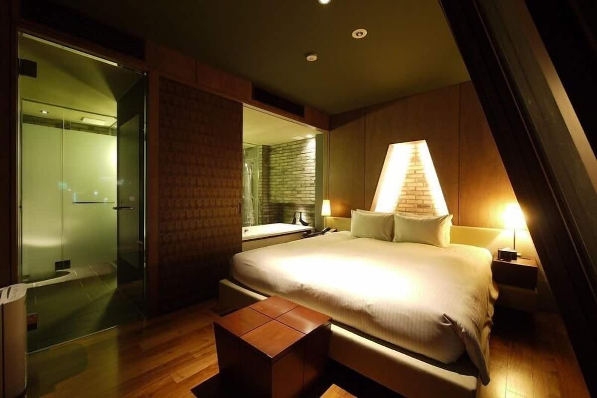 Une chambre d’hôtel moderne avec un grand lit, une douche à parois de verre et un plancher en bois.