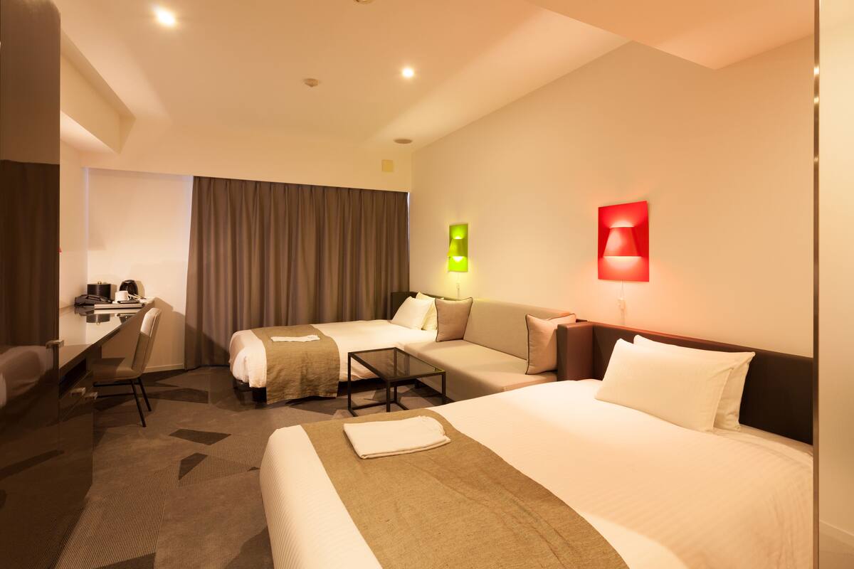 Une chambre d’hôtel équipée d’un lit, d’un bureau, d’une chaise, d’un canapé et de deux lampes fixées au mur.
