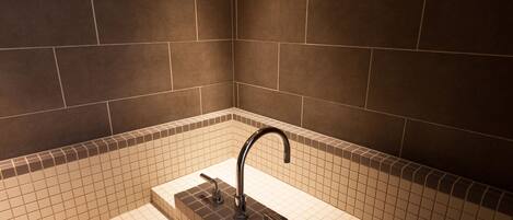 A bathroom with dark brown tiled walls, a white tiled floor, and a black faucet.