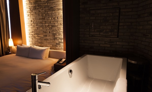 A modern hotel room with a large bed, a white bathtub, and a brick wall. - Shibuya Granbell hotel (Tokyo)