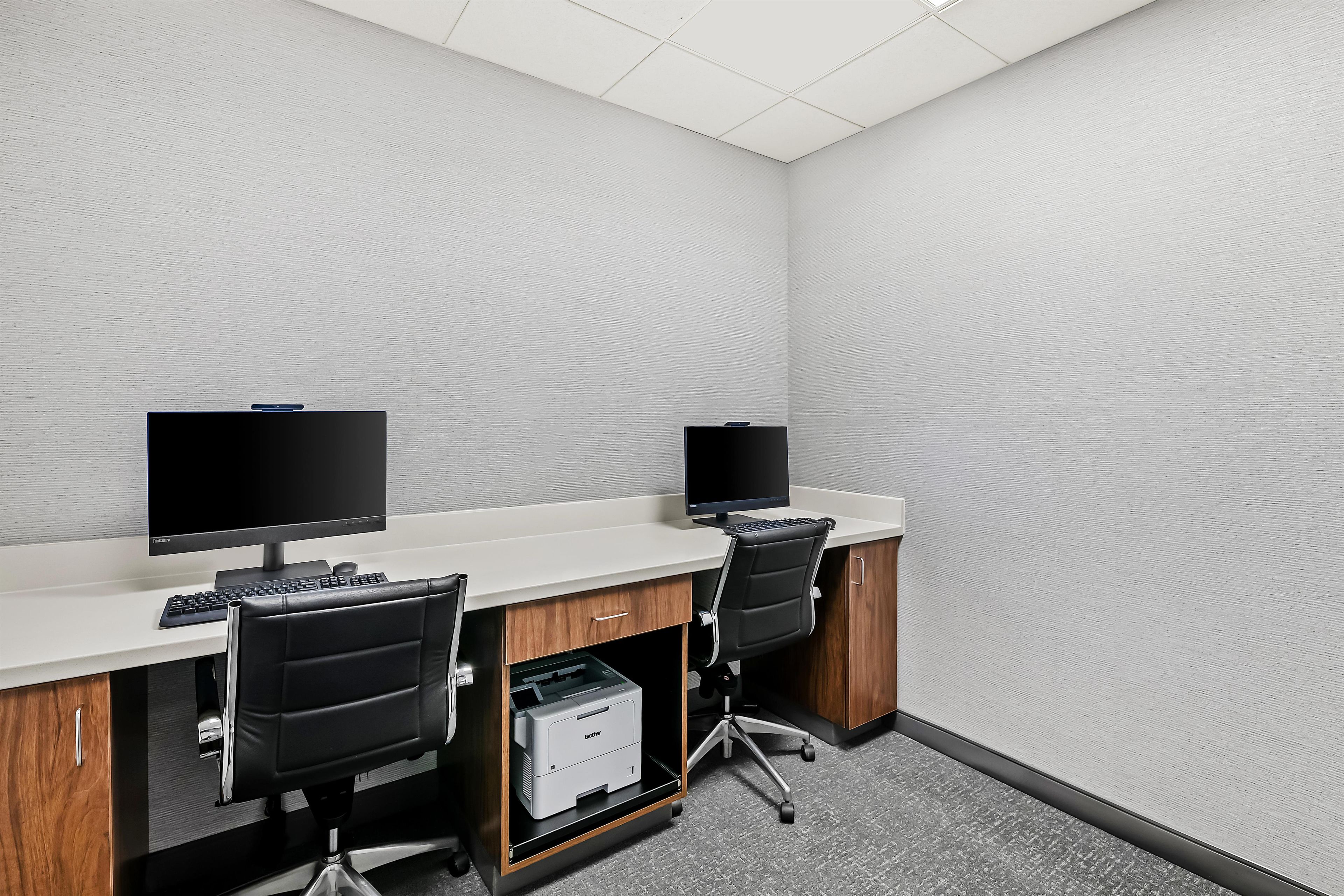 Une salle de conférence équipée de deux bureaux, chacun comprenant un écran d’ordinateur, un clavier et une chaise. Une imprimante est posée sur le sol.