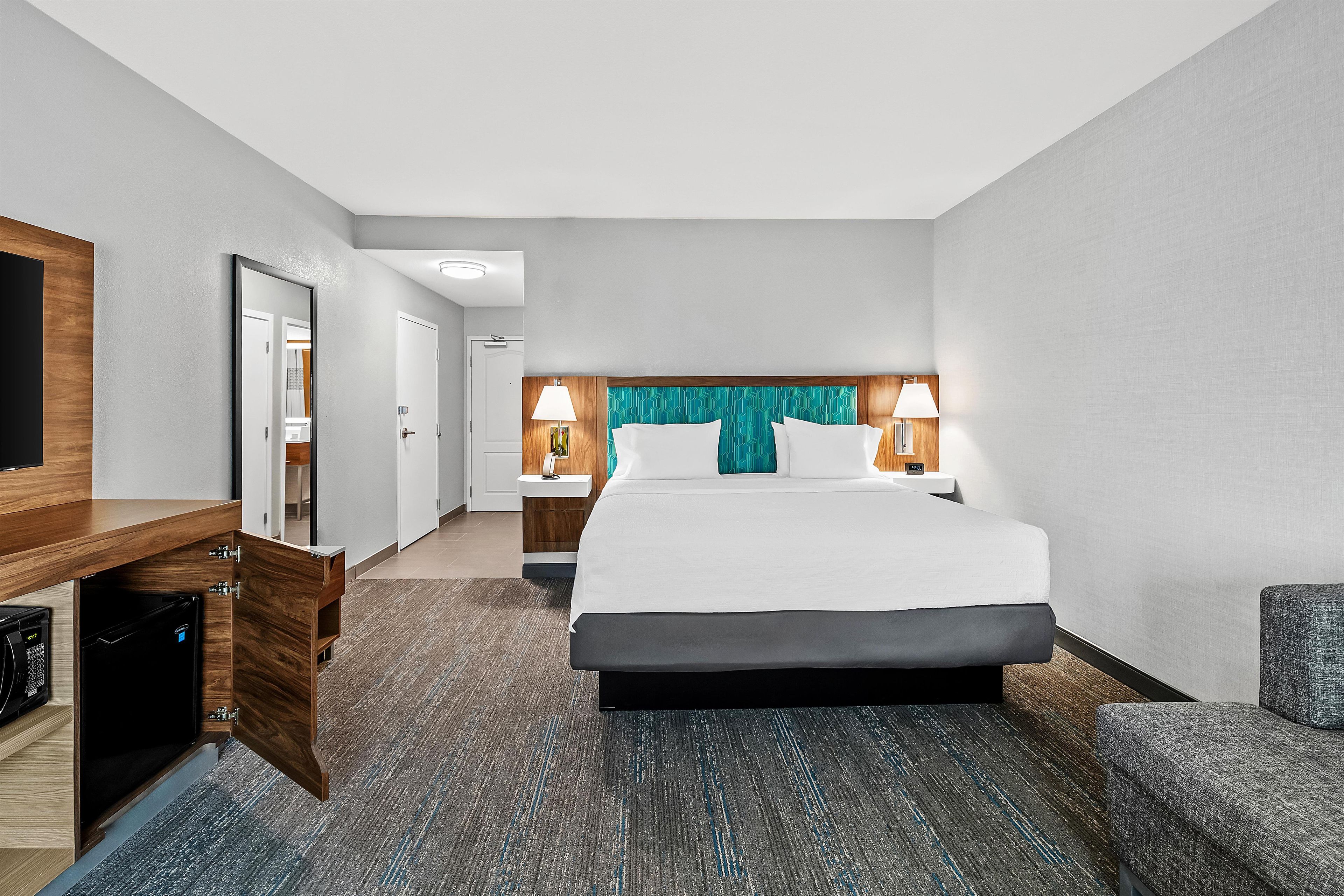 A hotel room with a bed, bedside tables, a desk, a chair, and a television.