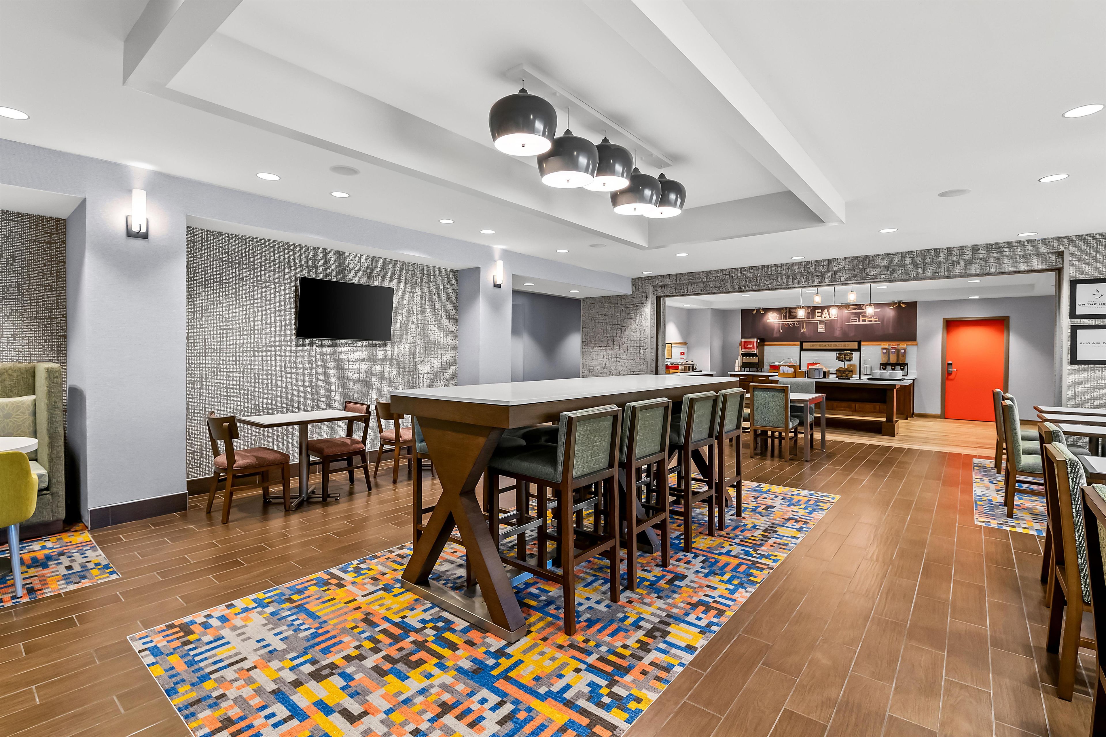 Un moderno vestíbulo de hotel con zona de bar, asientos y cocina visible a través de un umbral abierto.