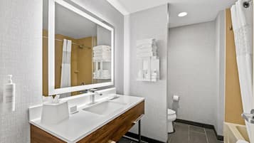 A modern bathroom with a double sink vanity, a large mirror, a toilet, and a shower area.